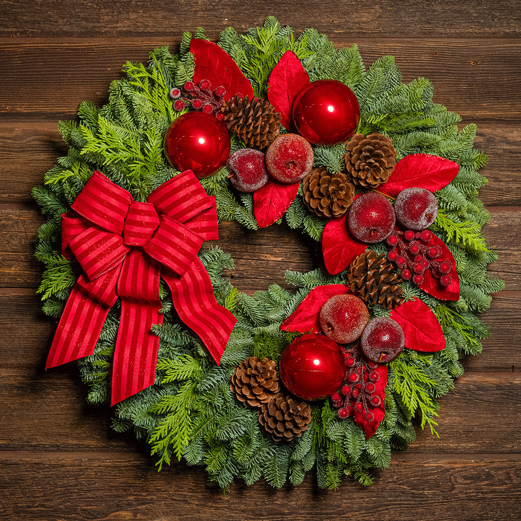 Christmas wreath with red berries, pine cones, and a red bow on a wooden background