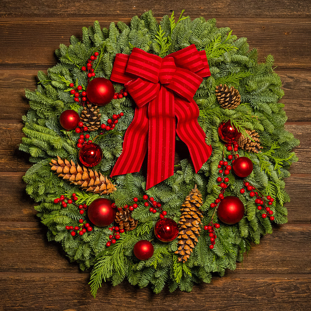 Christmas wreath with red bow, pine cones, and berries on a wooden background