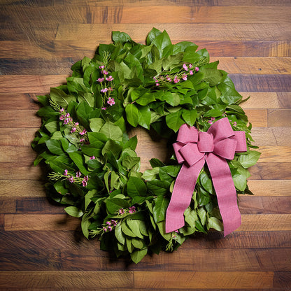 Green wreath with pink bow on a wooden surface