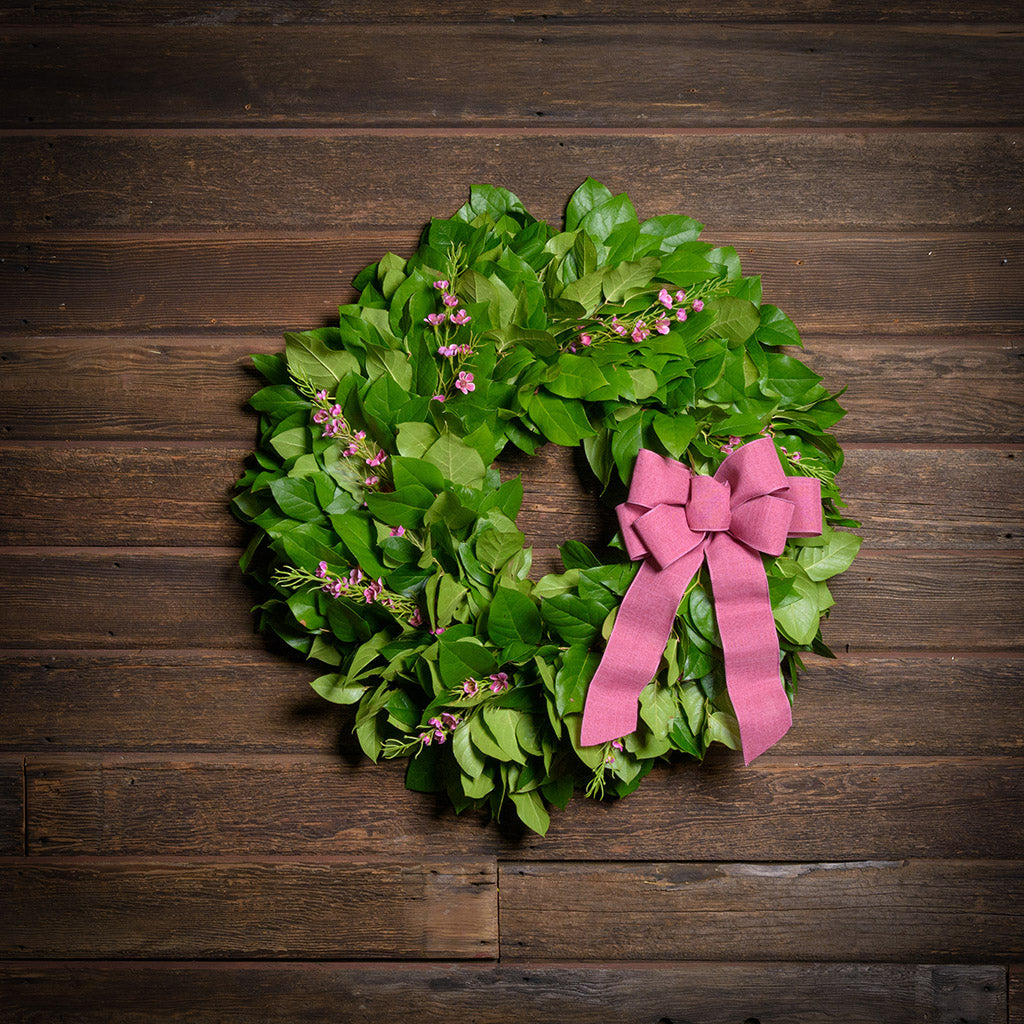 Green wreath with pink bow on a wooden background