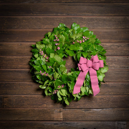 Green wreath with pink bow on a wooden background