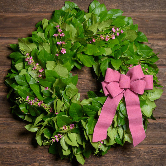Green leaf wreath with pink flowers and a pink bow on a wooden background