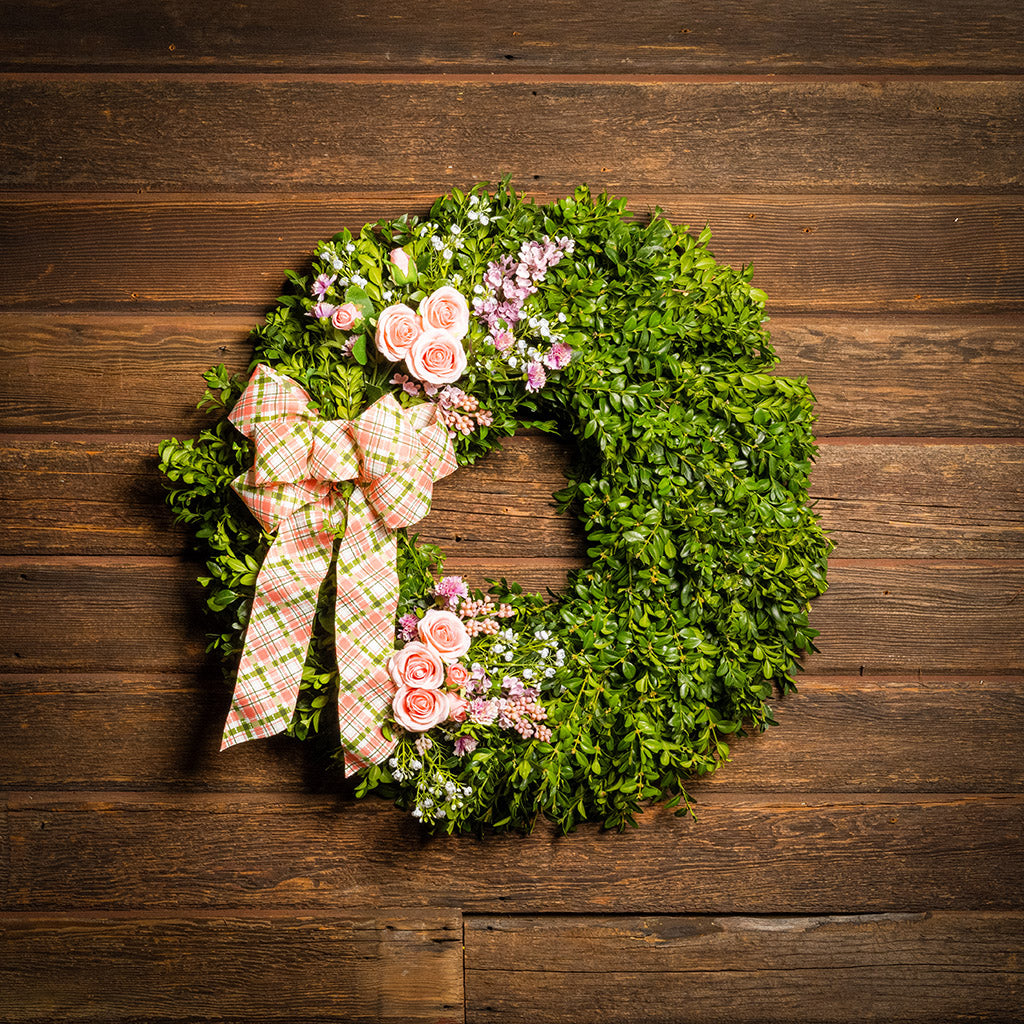 Fresh boxwood with faux lavender, peach roses, lilac, and small faux white baby’s breath flowers with a coral, cream, and green plaid bow