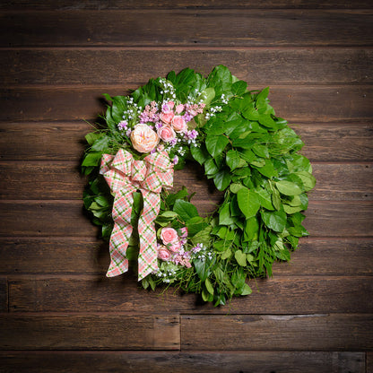 Green leaf wreath with pink flowers and a plaid bow on a wooden background