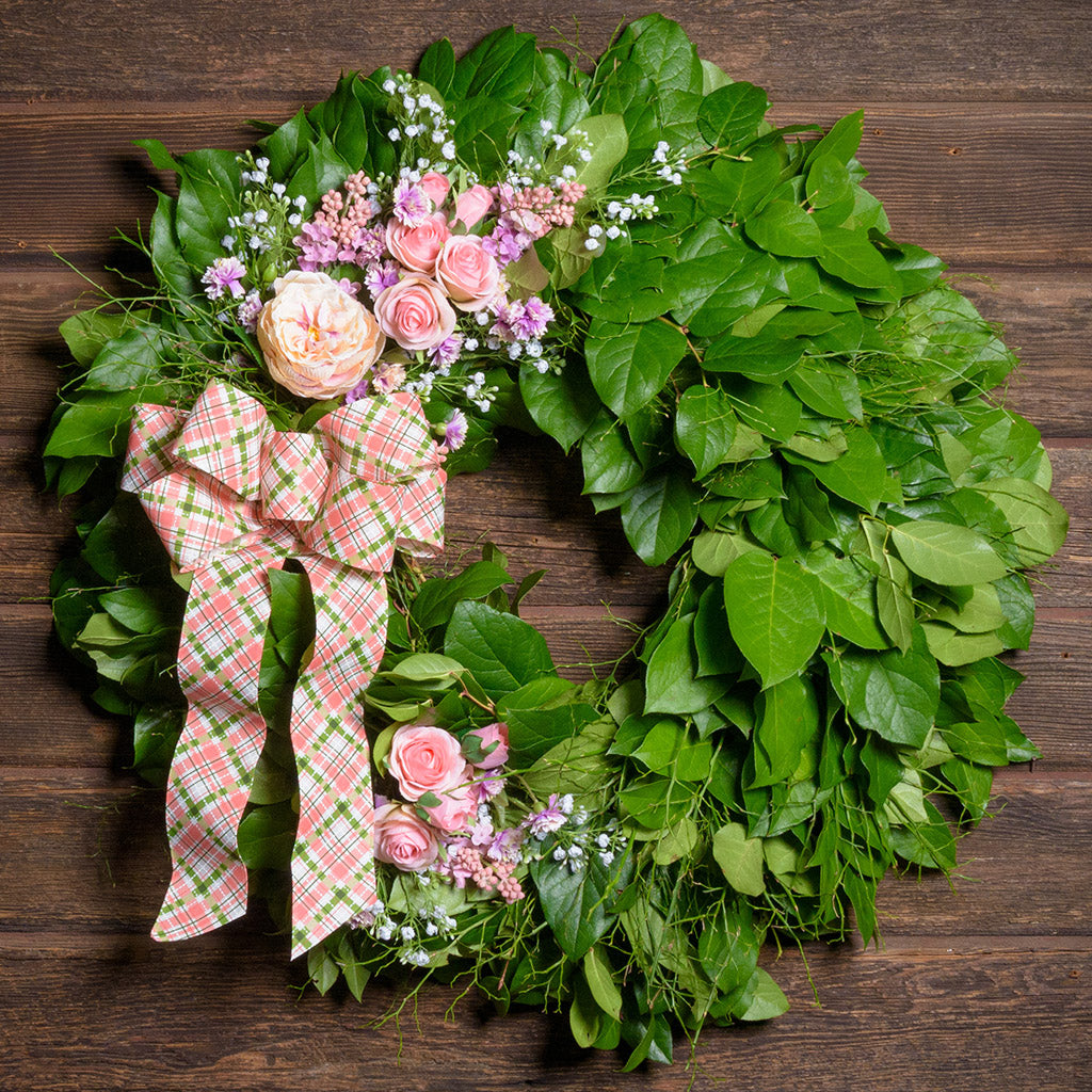Floral wreath with pink flowers and a plaid bow on a wooden background