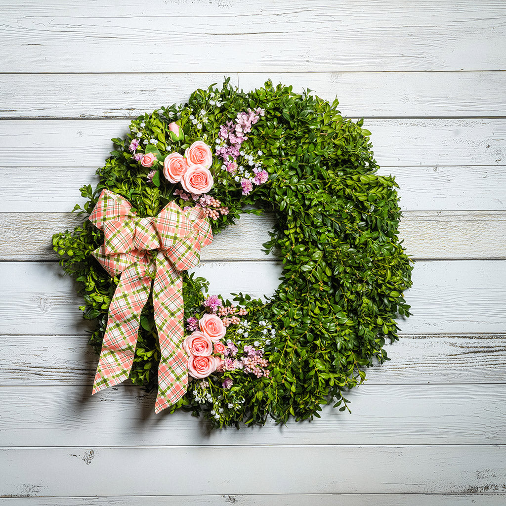 Fresh boxwood with faux lavender, peach roses, lilac, and small faux white baby’s breath flowers with a coral, cream, and green plaid bow