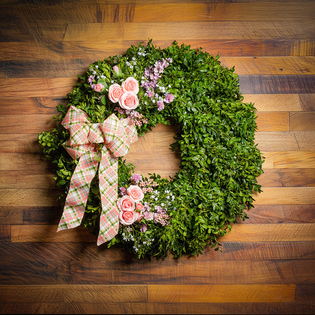 Fresh boxwood with faux lavender, peach roses, lilac, and small faux white baby’s breath flowers with a coral, cream, and green plaid bow