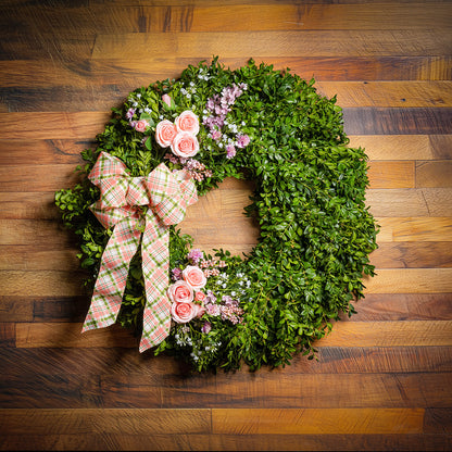 Fresh boxwood with faux lavender, peach roses, lilac, and small faux white baby’s breath flowers with a coral, cream, and green plaid bow