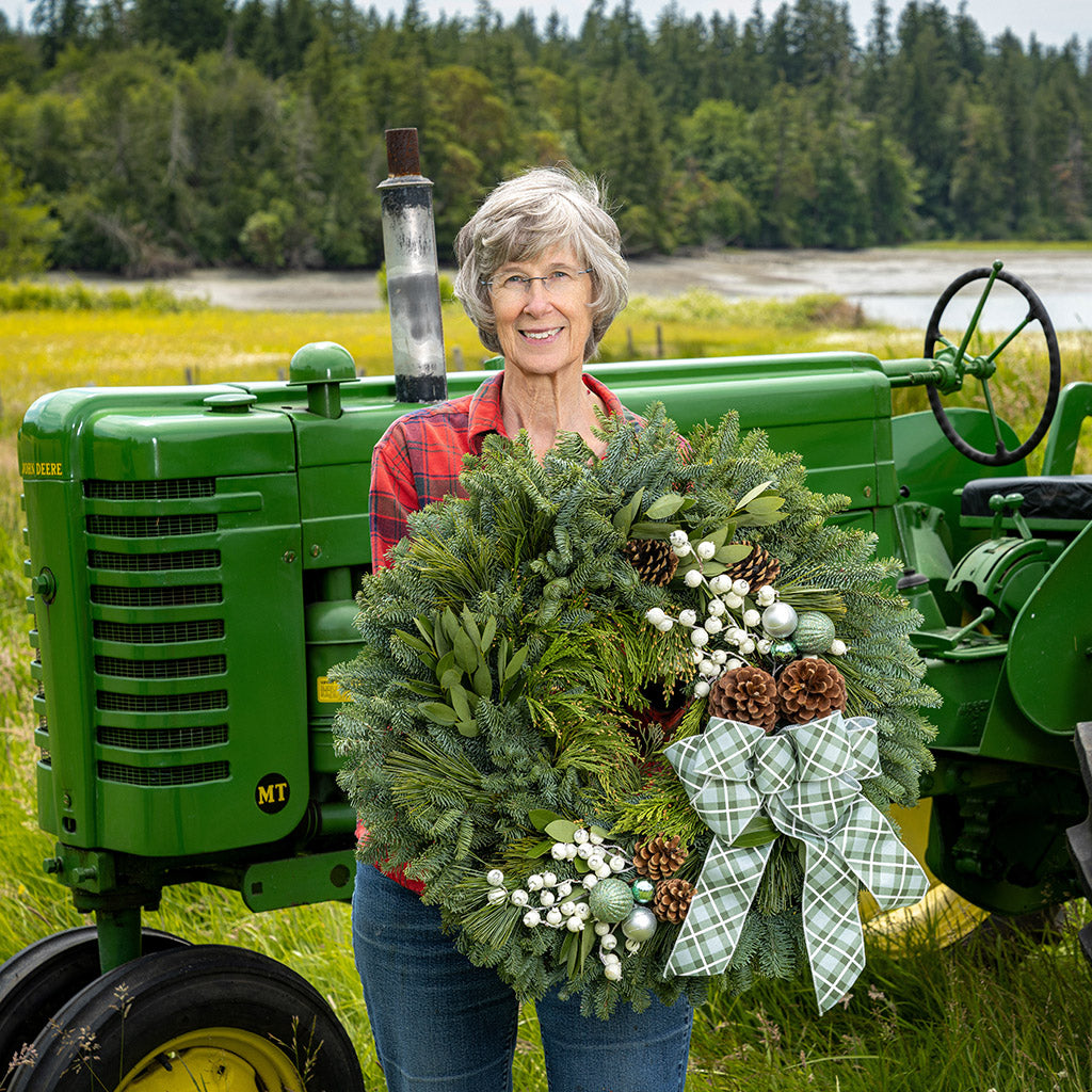 Woman holding a wreath in front of a green tractor with a forest background