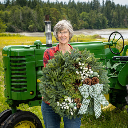 Woman holding a wreath in front of a green tractor with a forest background