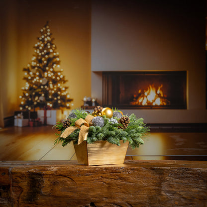 Decorative Christmas arrangement with ornaments on a wooden surface in front of a fireplace and tree.