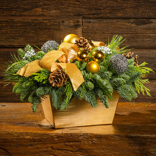 Decorative Christmas arrangement with greenery, gold ornaments, and a bow on a wooden surface.
