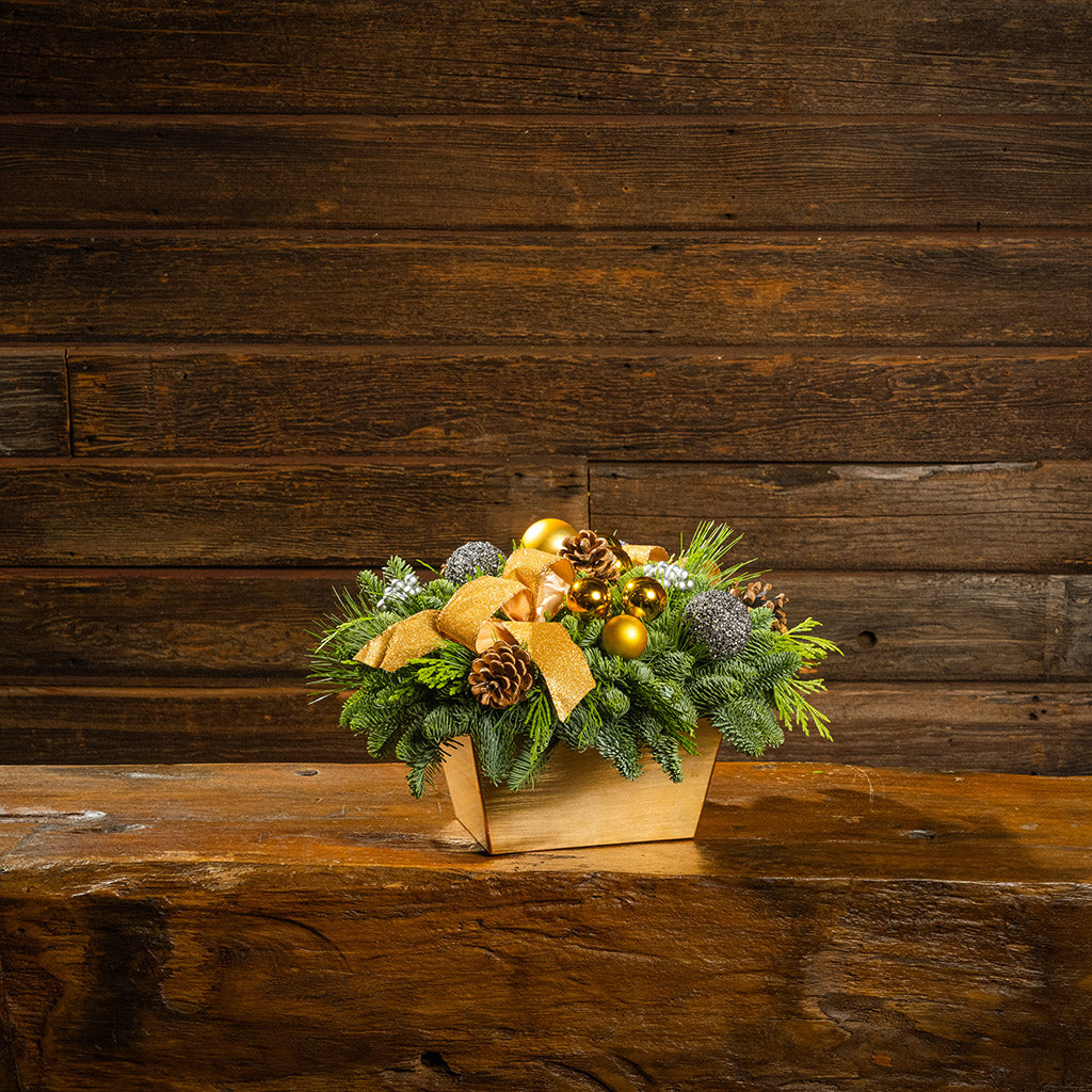 Decorative Christmas arrangement with greenery, gold ribbons, and ornaments on a wooden surface and background.