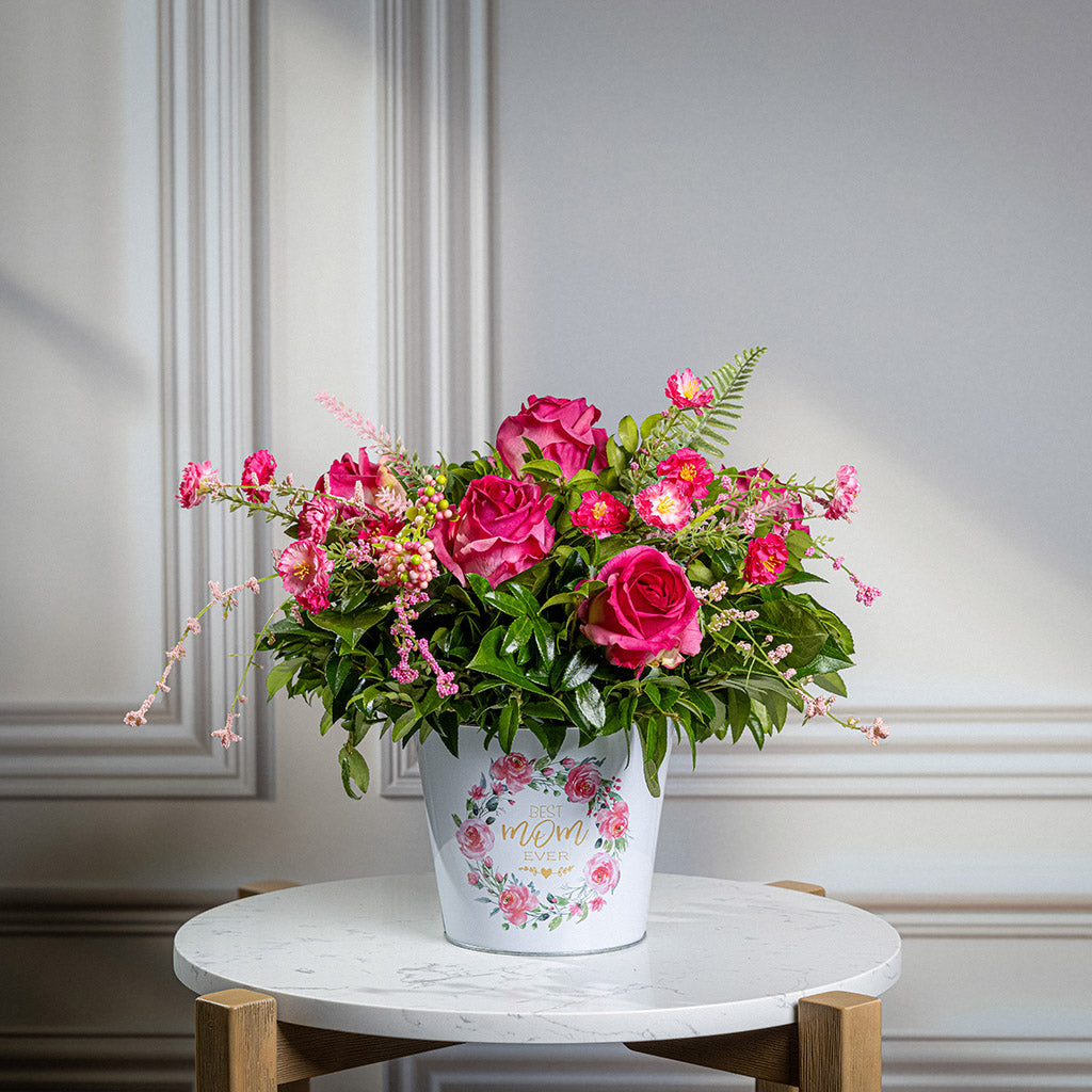 Fresh salal and green huckleberry with faux dogwood flowers and faux pink roses in a metal white floral container