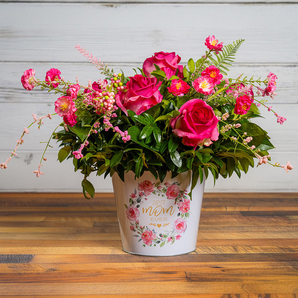 Fresh salal and green huckleberry with faux dogwood flowers and faux pink roses in a metal white floral container