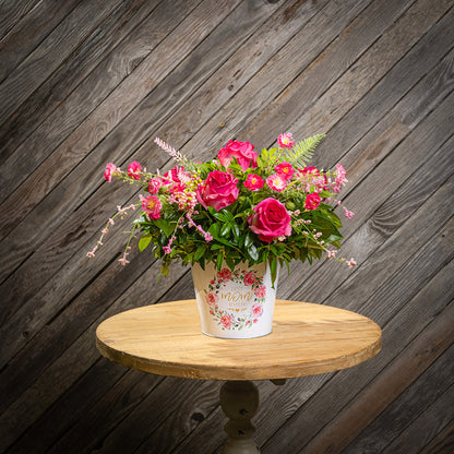 Fresh salal and green huckleberry with faux dogwood flowers and faux pink roses in a metal white floral container