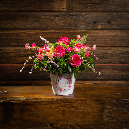 Fresh salal and green huckleberry with faux dogwood flowers and faux pink roses in a metal white floral container