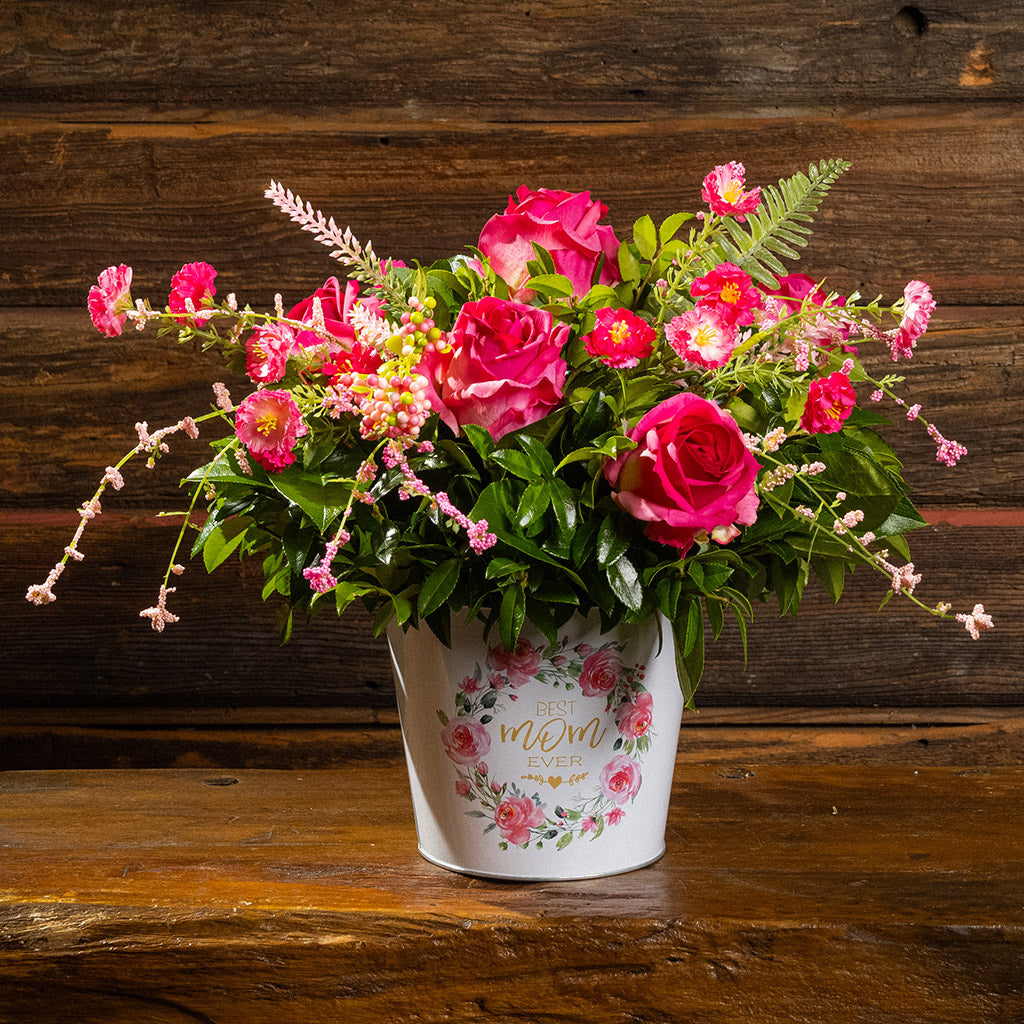 Fresh salal and green huckleberry with faux dogwood flowers and faux pink roses in a metal white floral container