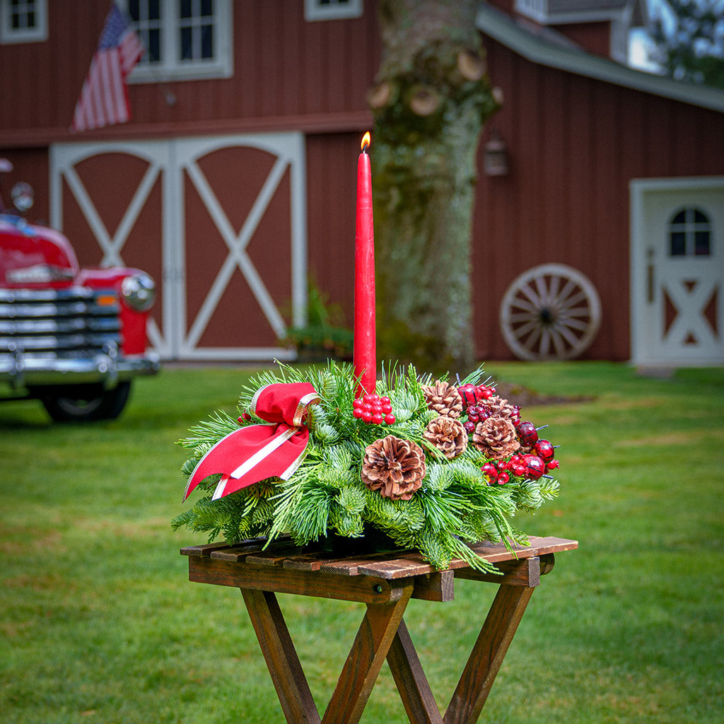 Christmas centerpiece with pine cones, gold balls and red berries with red velveteen bows and a red taper candle