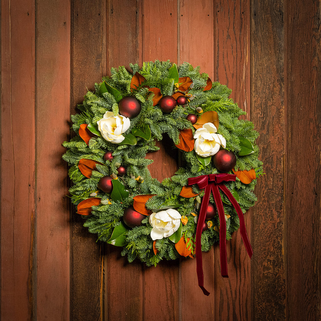 Christmas wreath with red berries, white flowers, and a red ribbon on a wooden door.