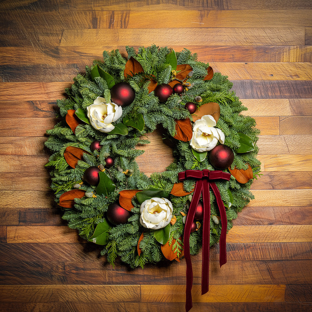 Decorative Christmas wreath with red ornaments and a red ribbon on a wooden background