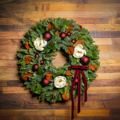 Decorative Christmas wreath with red ornaments and a red ribbon on a wooden background