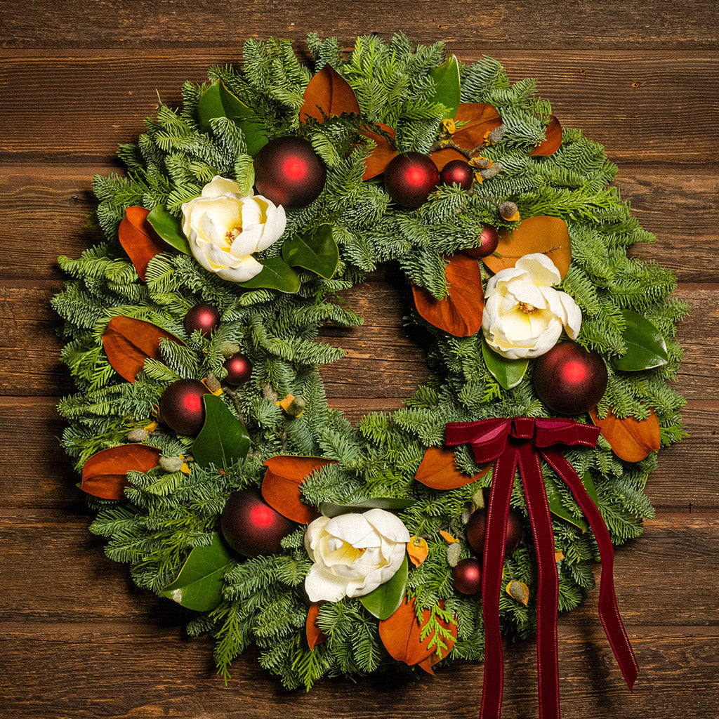 Decorative Christmas wreath with red ornaments and white flowers on a wooden background