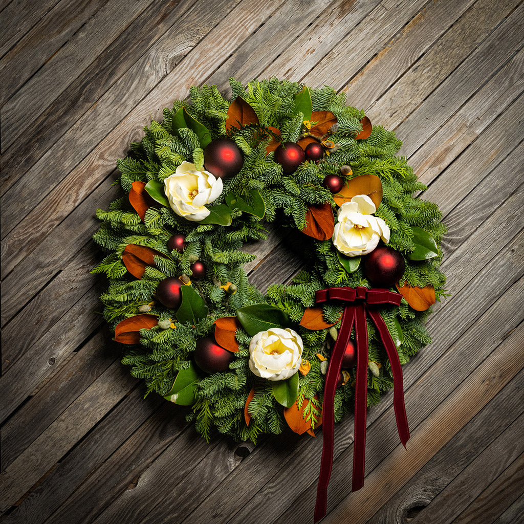 Christmas wreath with red berries, white flowers, and a red ribbon on a wooden background