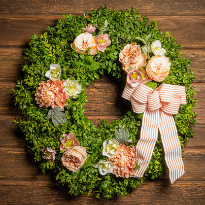 Fresh boxwood with faux peachy mums, faux peachy roses, and faux cream hellebore flowers with a peach and white striped bow