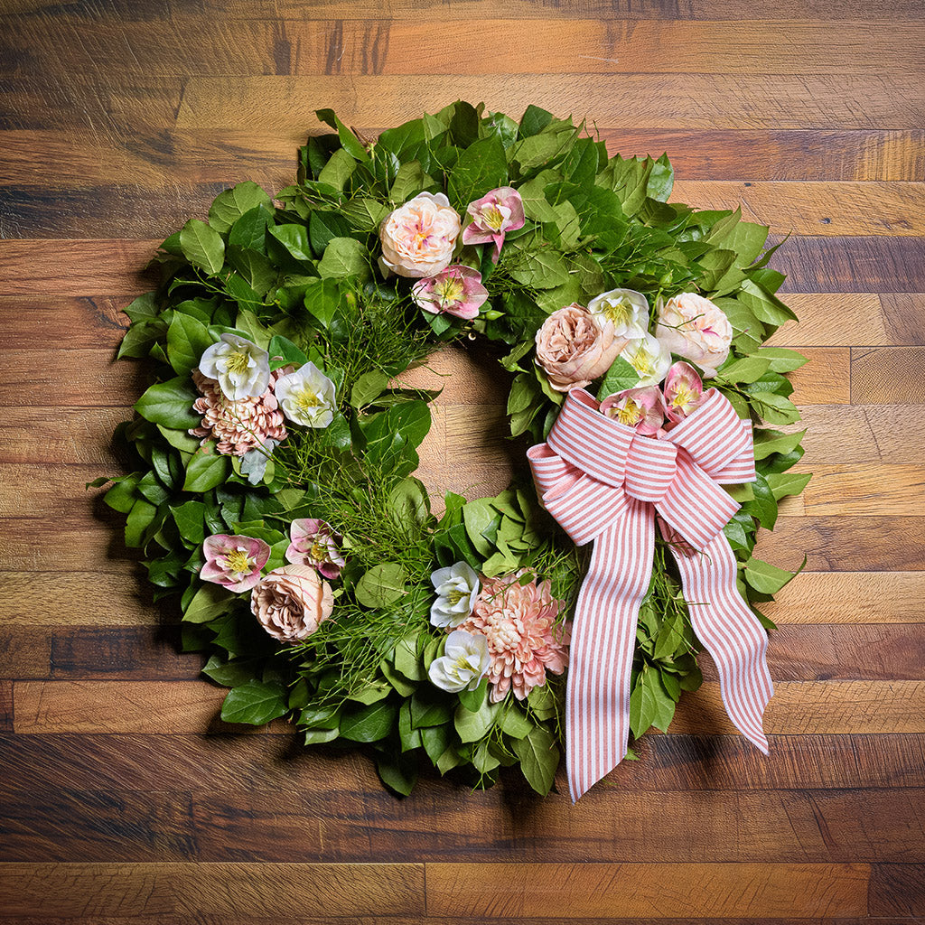 Green wreath with pink flowers and a striped bow on a wooden surface