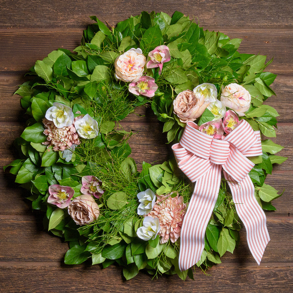Decorative wreath with flowers and a pink bow on a wooden background