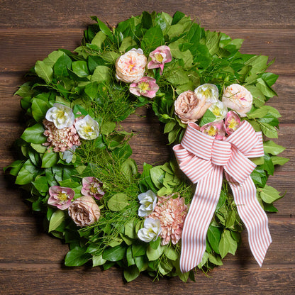 Decorative wreath with flowers and a pink bow on a wooden background