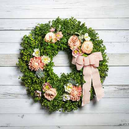 Fresh boxwood with faux peachy mums, faux peachy roses, and faux cream hellebore flowers with a peach and white striped bow