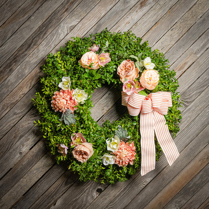 Fresh boxwood with faux peachy mums, faux peachy roses, and faux cream hellebore flowers with a peach and white striped bow