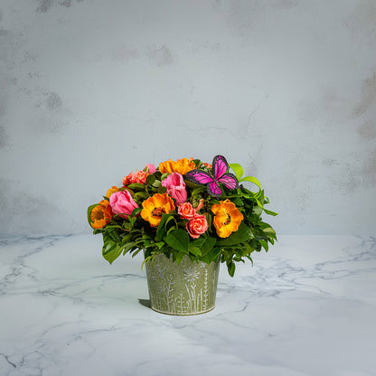 Fresh salal and green huckleberry with faux orange poppies, faux pink tulips, faux peach roses, a bright green bow, and a pink butterfly in a metal green container