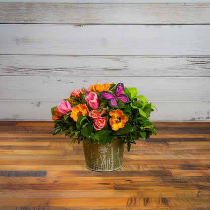 Fresh salal and green huckleberry with faux orange poppies, faux pink tulips, faux peach roses, a bright green bow, and a pink butterfly in a metal green container