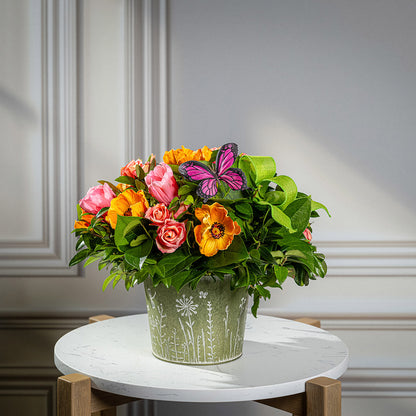 Fresh salal and green huckleberry with faux orange poppies, faux pink tulips, faux peach roses, a bright green bow, and a pink butterfly in a metal green container