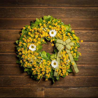 Fresh salal and sweet huckleberry with assorted faux small yellow daisies, faux white wax flowers, and faux white daisies with a sage-green and ivory striped bow