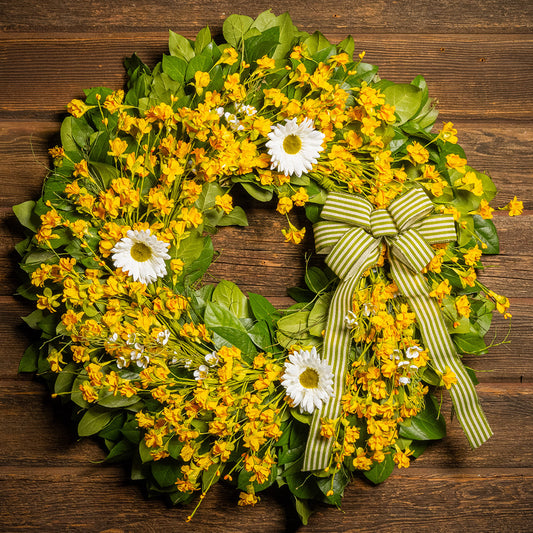 Fresh salal and sweet huckleberry with assorted faux small yellow daisies, faux white wax flowers, and faux white daisies with a sage-green and ivory striped bow