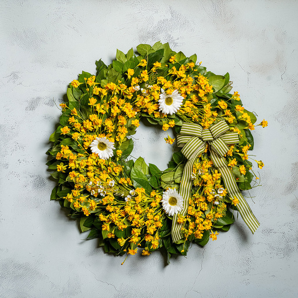 Fresh salal and sweet huckleberry with assorted faux small yellow daisies, faux white wax flowers, and faux white daisies with a sage-green and ivory striped bow