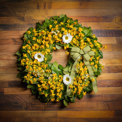 Fresh salal and sweet huckleberry with assorted faux small yellow daisies, faux white wax flowers, and faux white daisies with a sage-green and ivory striped bow