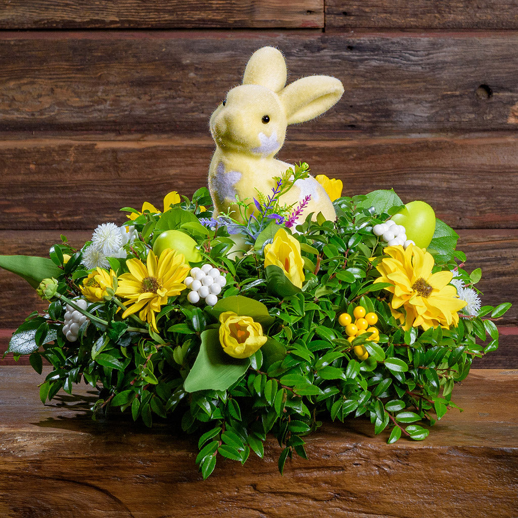Floral arrangement with yellow flowers and a soft bunny toy on a wooden surface.