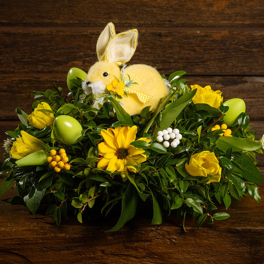 Fresh salal and green huckleberry with yellow berries, white berries, faux daisies, faux yellow tulips, faux light-green eggs, and a yellow rabbit