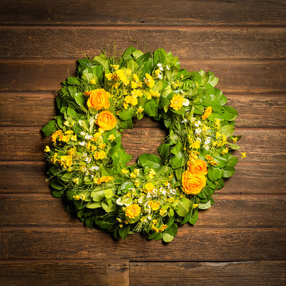 Fresh salal and sweet huckleberry with faux orange and yellow ranunculus, white wax flowers, and other mixed yellow flowers