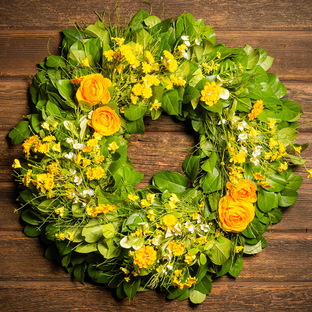 Fresh salal and sweet huckleberry with faux orange and yellow ranunculus, white wax flowers, and other mixed yellow flowers