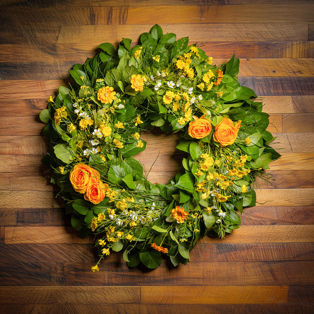 Fresh salal and sweet huckleberry with faux orange and yellow ranunculus, white wax flowers, and other mixed yellow flowers