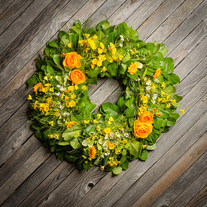 Fresh salal and sweet huckleberry with faux orange and yellow ranunculus, white wax flowers, and other mixed yellow flowers