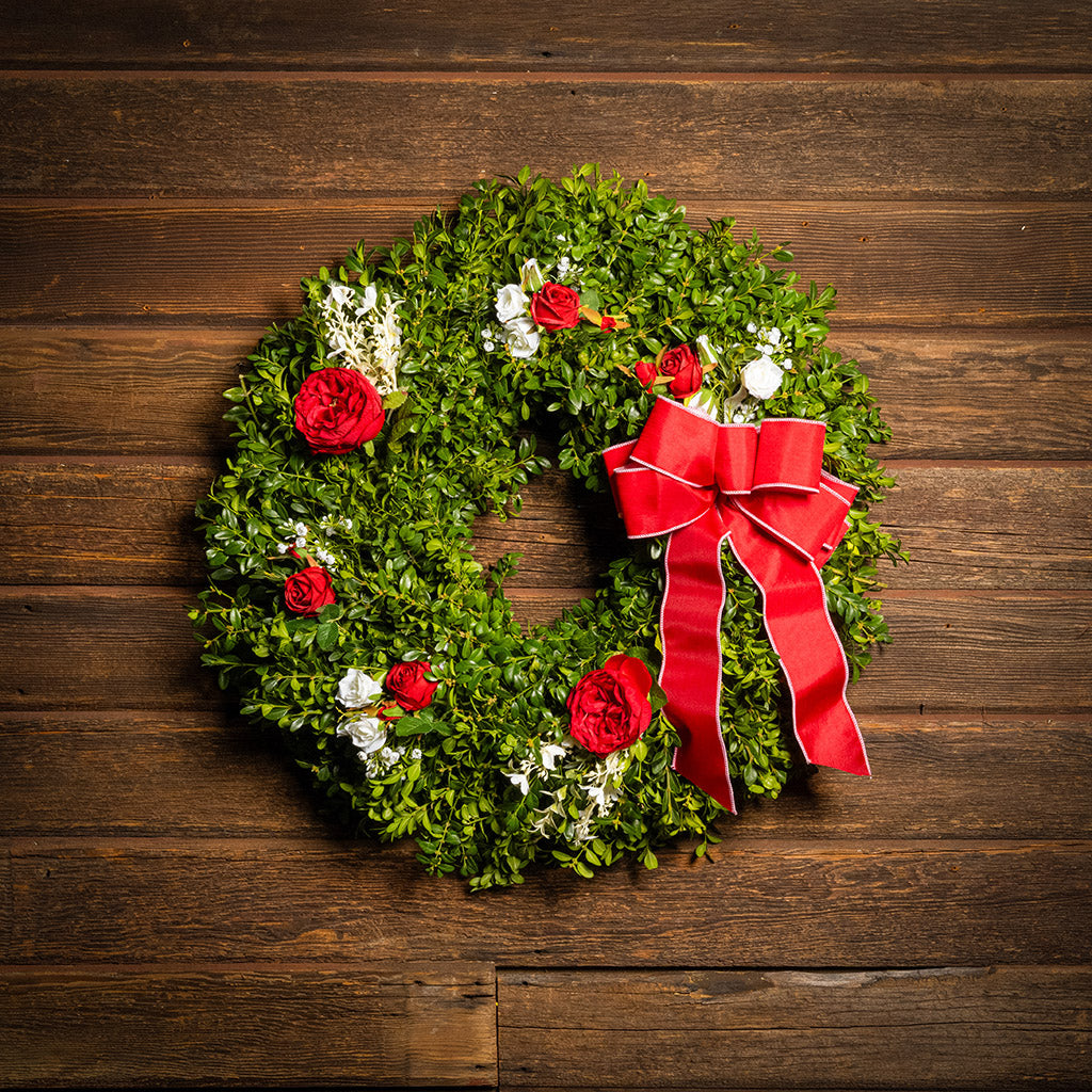 Fresh boxwood with faux red roses, faux white roses, and other faux white flowers with a red and pink-back bow