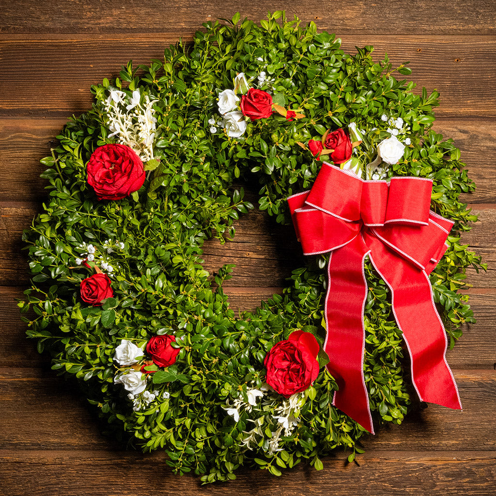 Fresh boxwood with faux red roses, faux white roses, and other faux white flowers with a red and pink-back bow