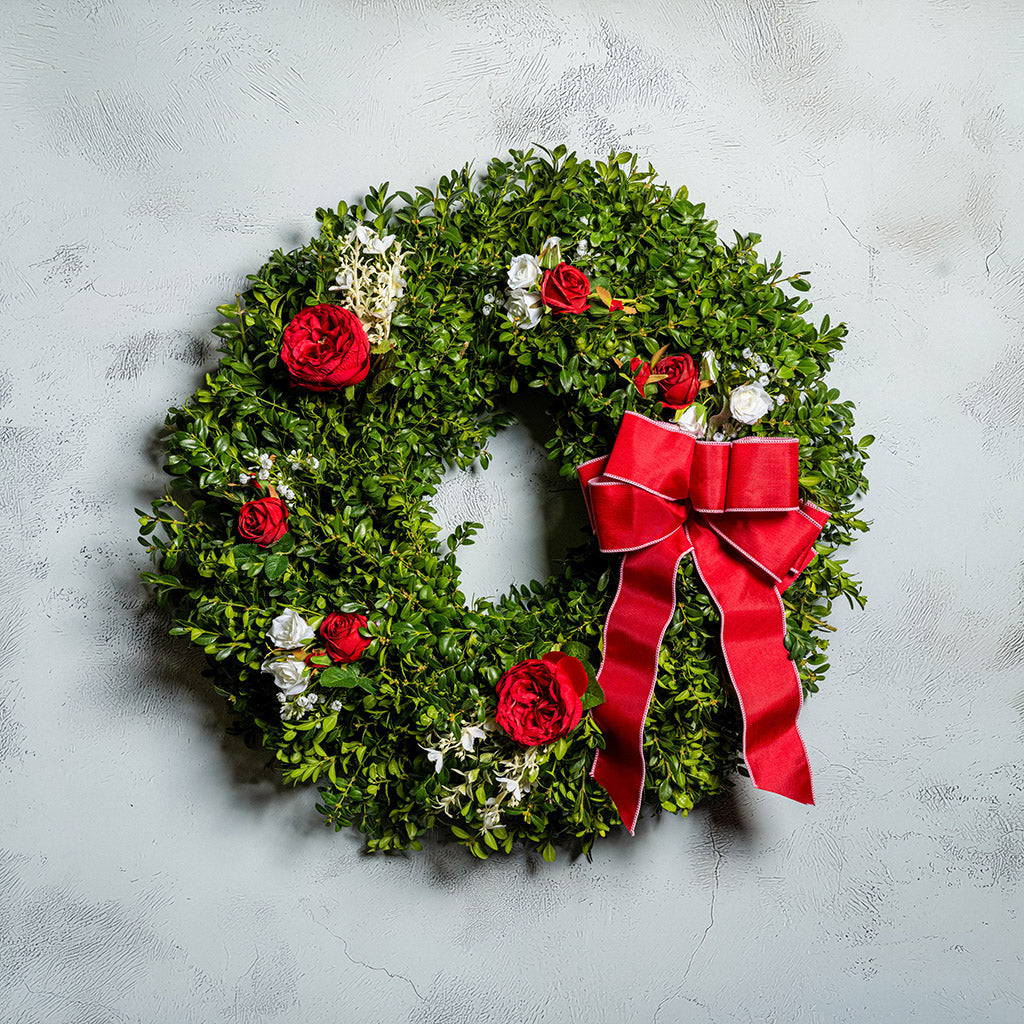 Fresh boxwood with faux red roses, faux white roses, and other faux white flowers with a red and pink-back bow